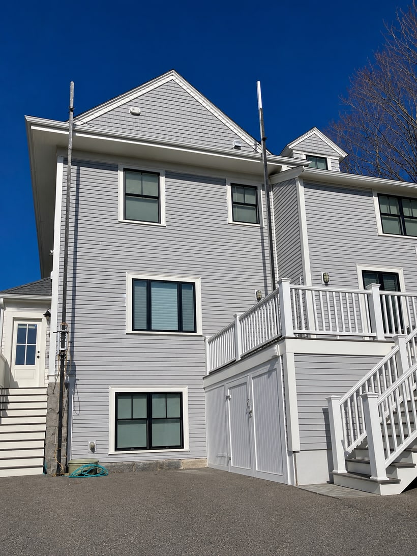 Exterior siding and trim painting on a multi-story home with gray siding, white trim, black windows, and deck railing