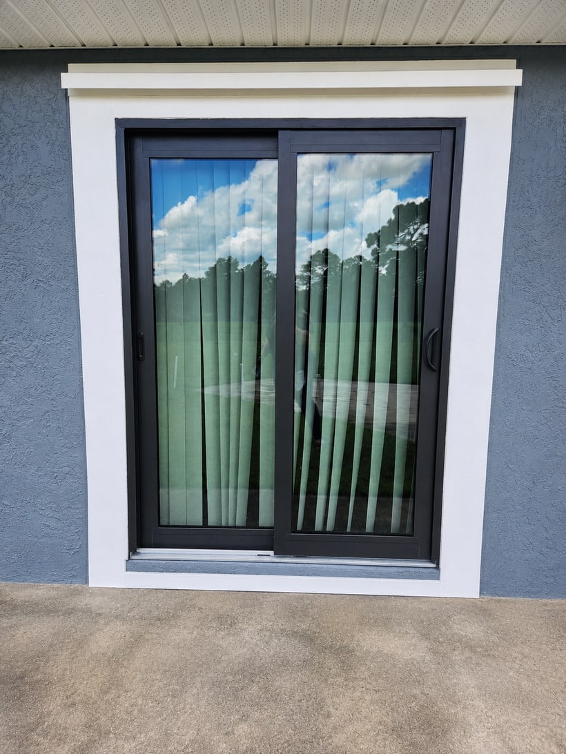 Installed black framed sliding glass patio door with clean white exterior trim on a stucco wall