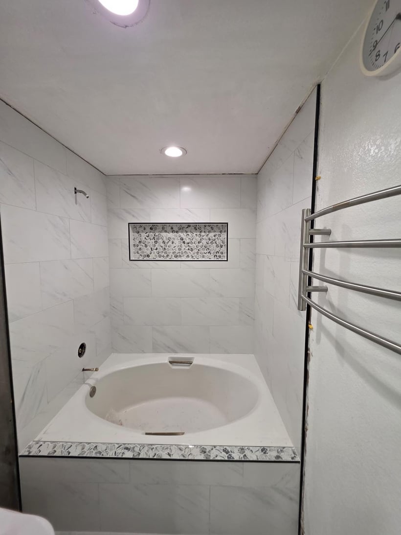 Finished white bathtub remodel with light wall tile and decorative niche